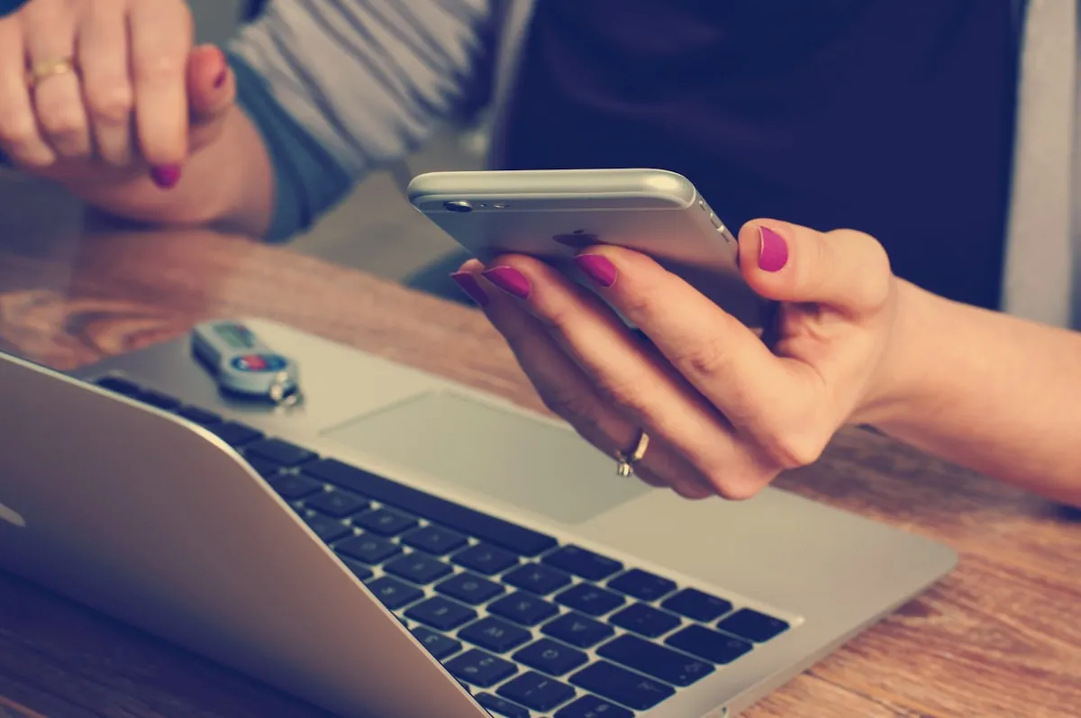 A person messaging on their phone while working at a laptop